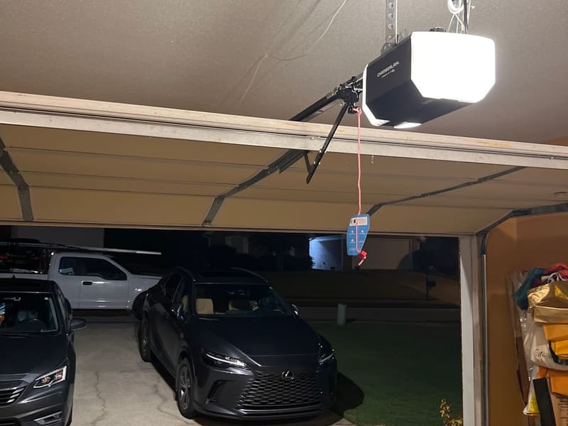 Garage door opener light on at night over two cars in an open garage