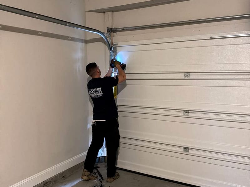 Swift Lift technician working on the vertical track beside a white sectional garage door