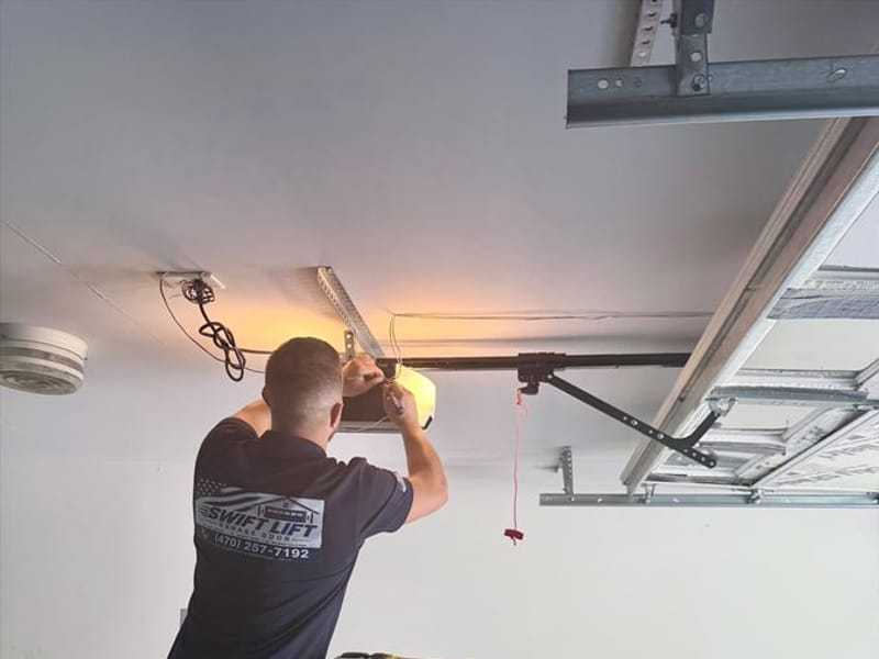 Swift Lift technician in a branded shirt working on a garage door opener mounted on the ceiling