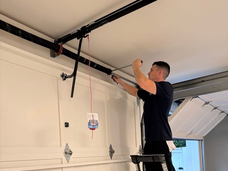 Swift Lift technician on a ladder working on the top section and hinges of a white garage door