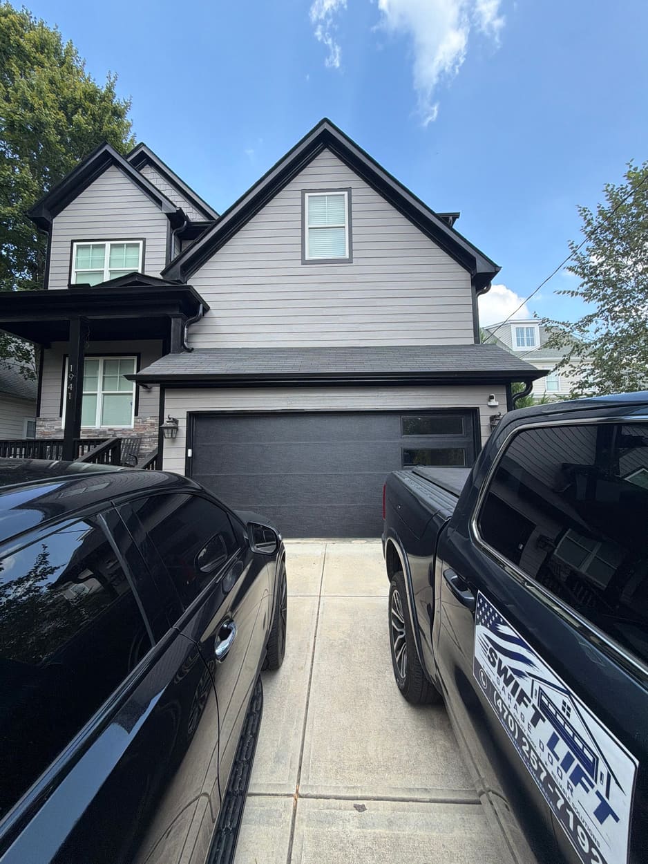 Modern dark flush-panel garage door with side glass on a gray two-story home, Swift Lift truck in the driveway