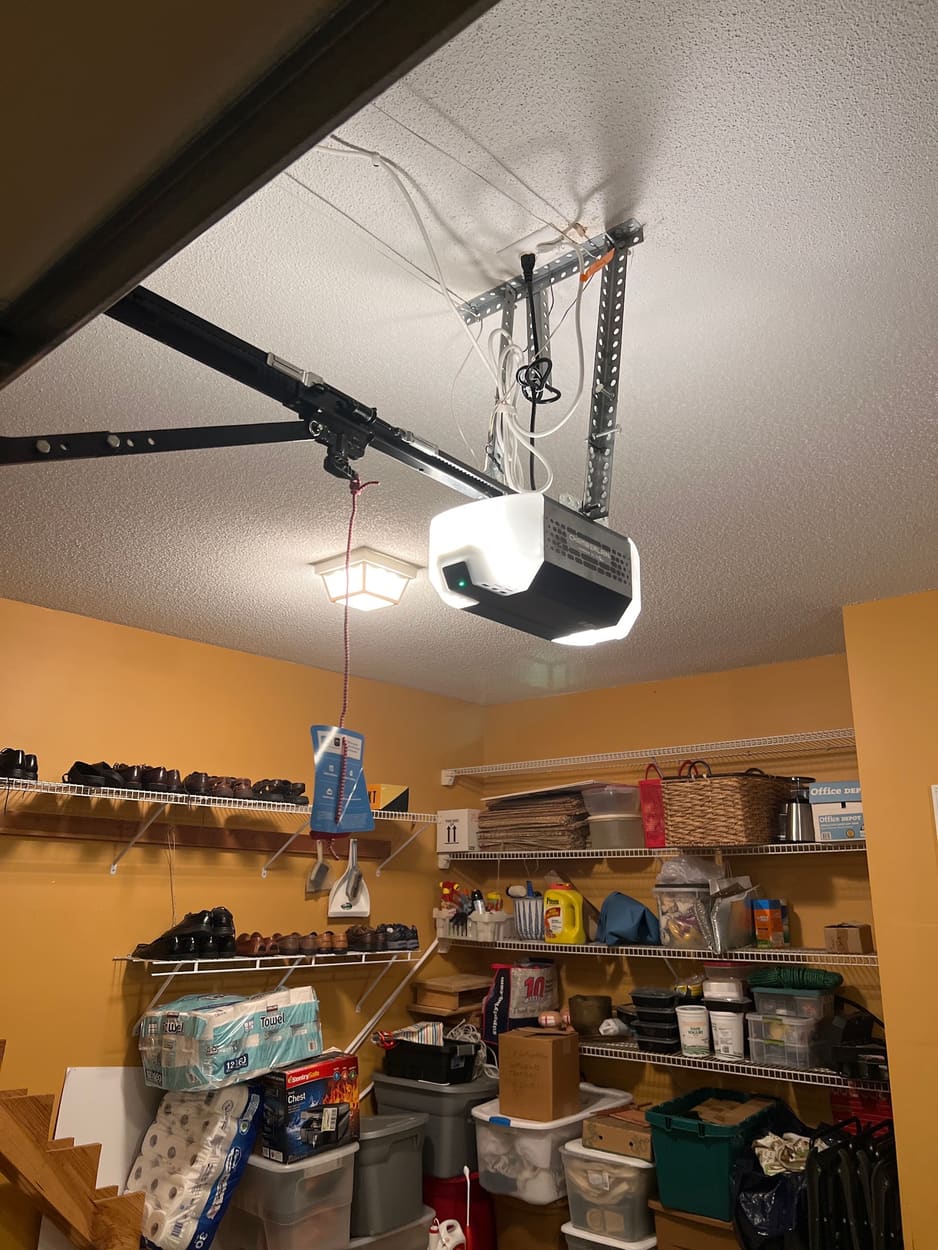 Garage door opener with its light on, installed on a garage ceiling