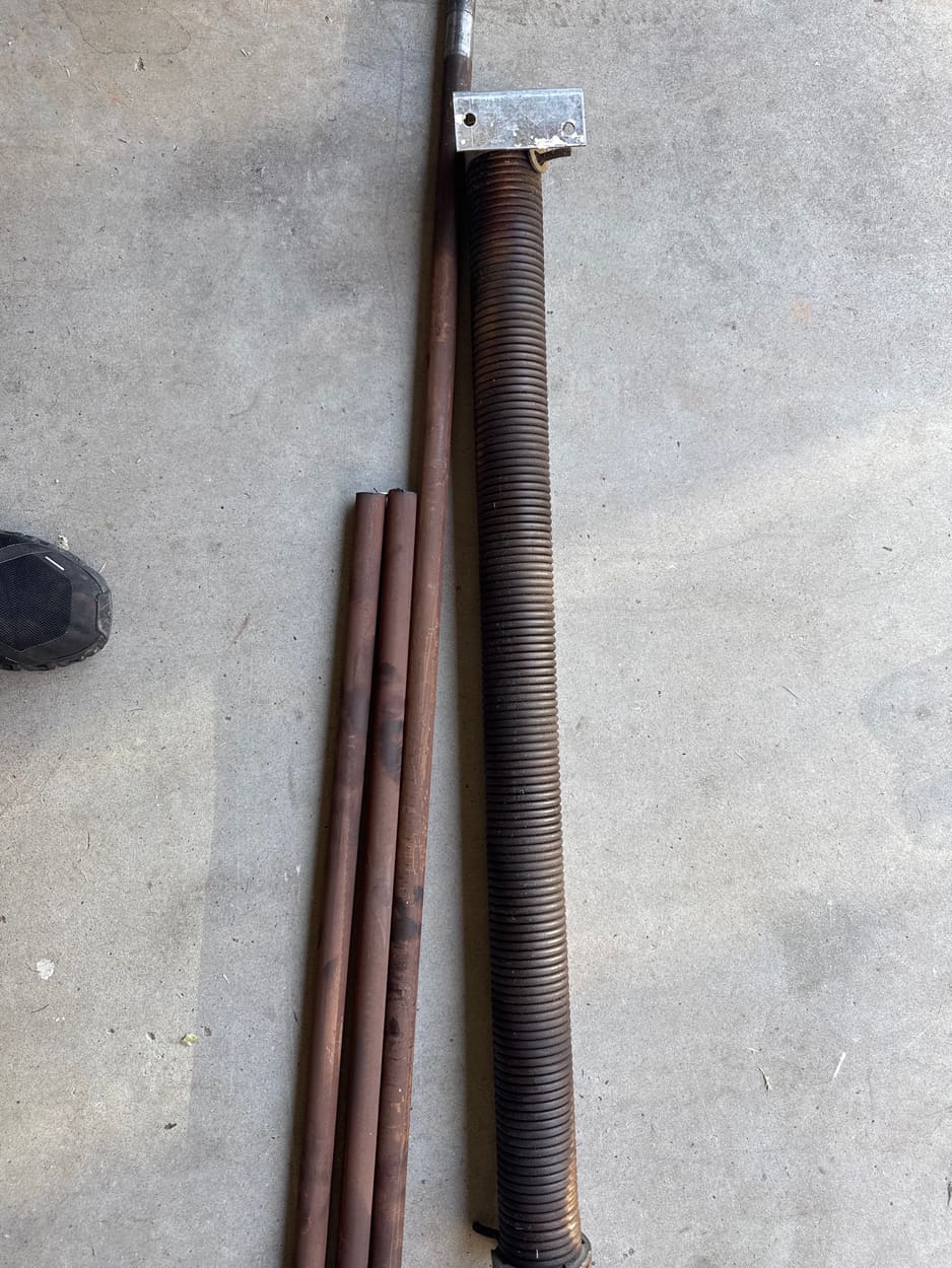 Old rusted garage door torsion springs and shaft laid on a driveway after being removed