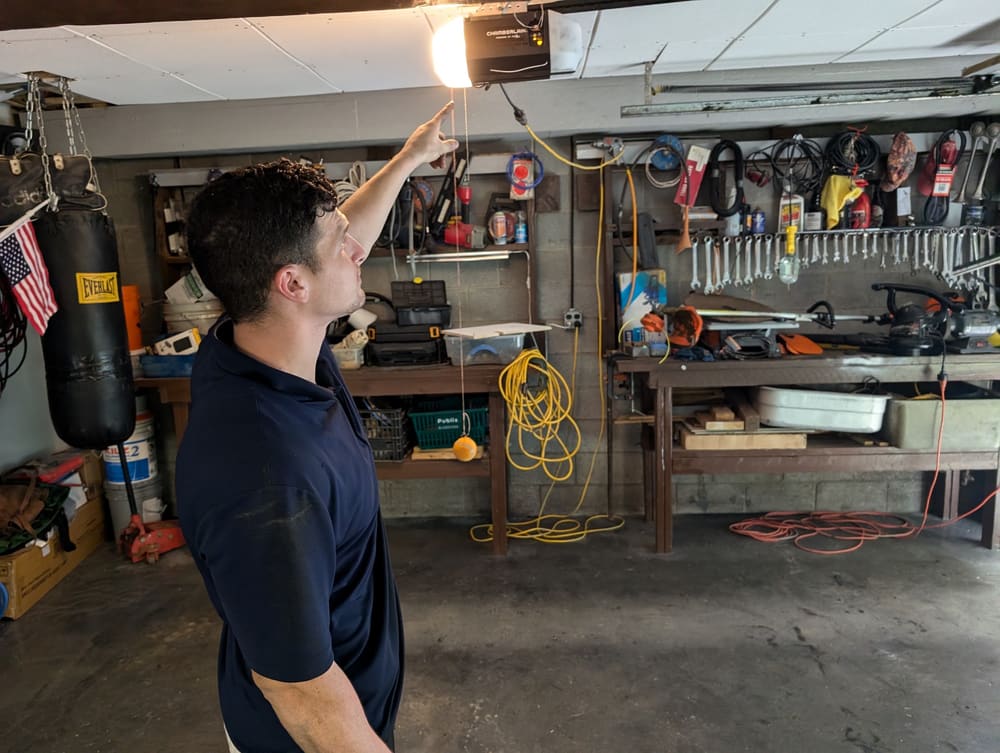 Swift Lift technician pointing out a garage door opener in a customer's workshop garage