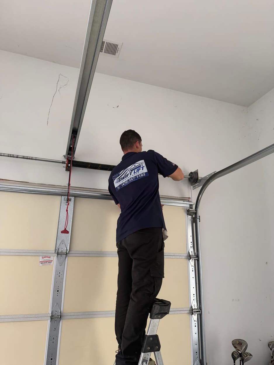 Swift Lift technician on a ladder working on the spring bar above an insulated garage door