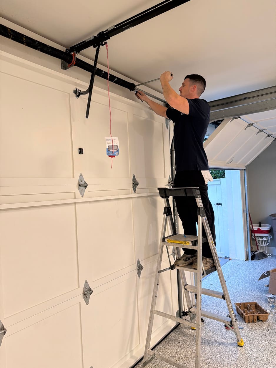 Swift Lift technician on a ladder working on the hardware at the top of a white carriage-style garage door