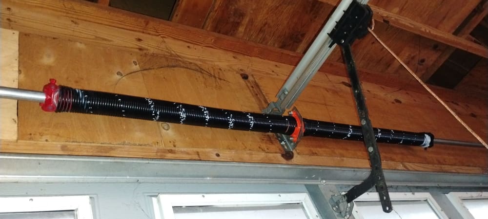 New black torsion spring mounted on a wood header above a garage door