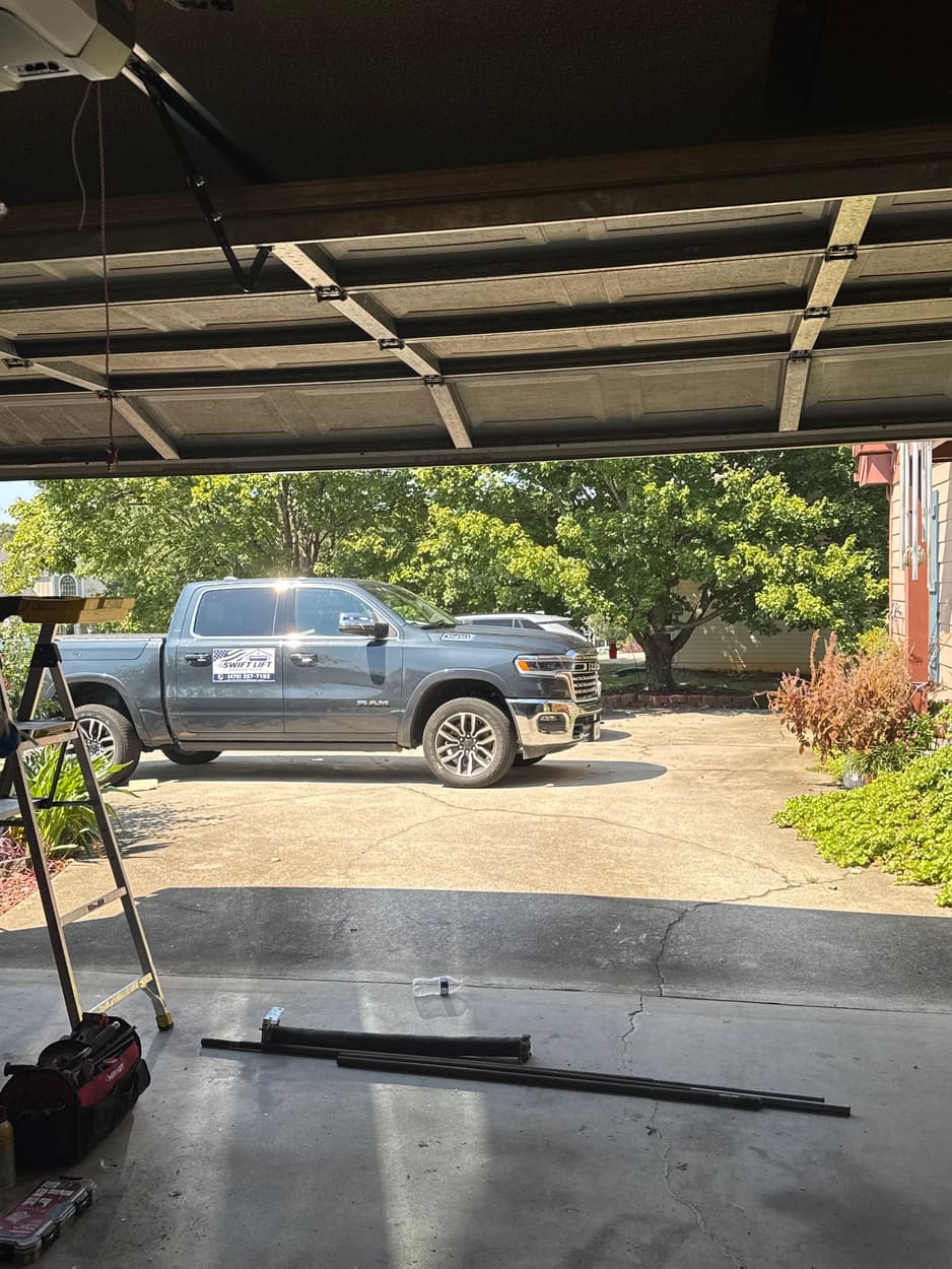 Swift Lift truck parked outside a customer's open garage with old spring parts on the floor