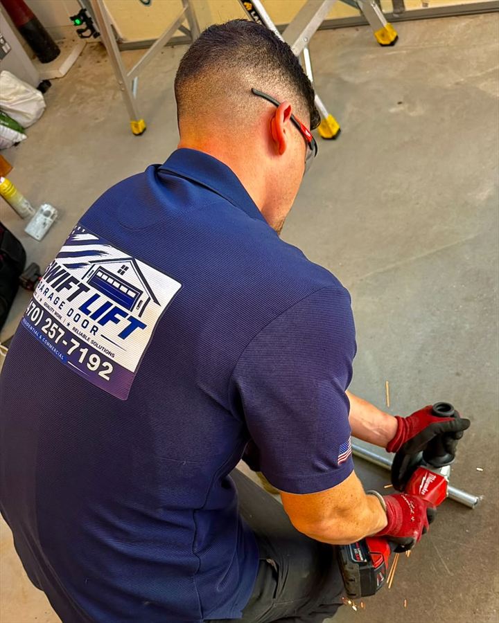 SwiftLift technician in branded uniform cutting a garage door torsion shaft to length with a grinder, wearing safety glasses and work gloves