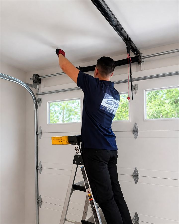 SwiftLift technician on a ladder fitting the torsion spring and rail assembly on a newly installed residential garage door