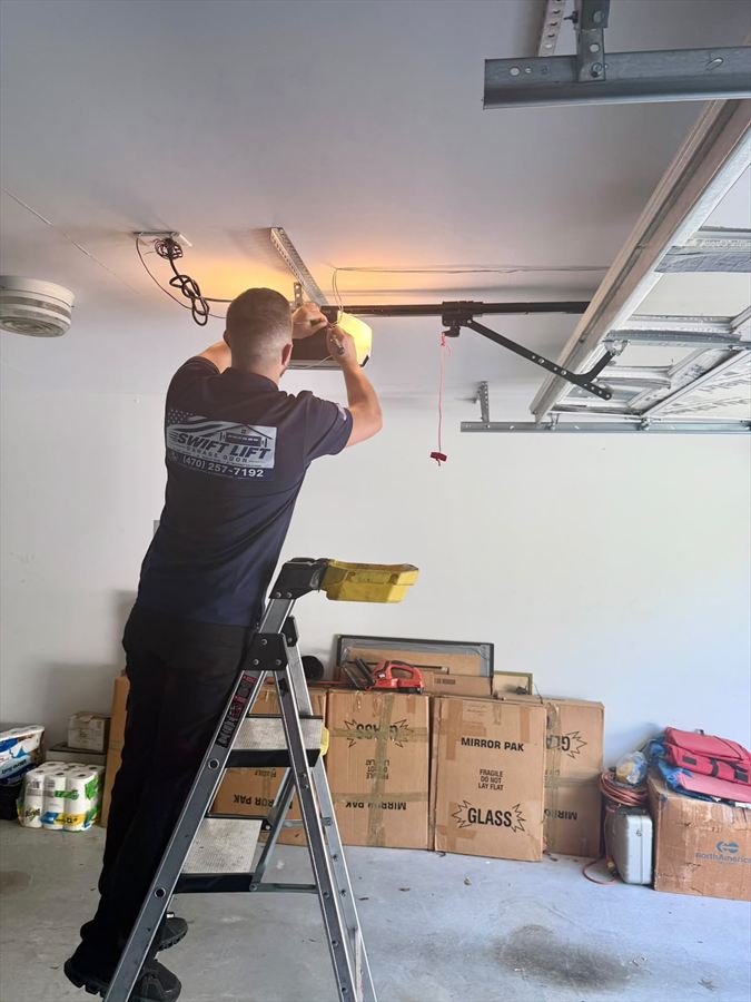 Swift Lift technician on a ladder installing a ceiling-mounted garage door opener