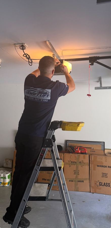 SwiftLift technician on a ladder servicing a garage door opener motor unit