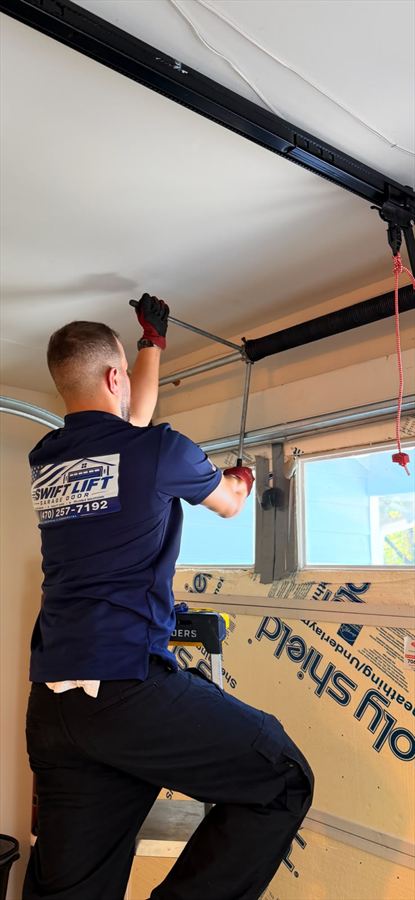 SwiftLift technician winding a new garage door torsion spring with winding bars